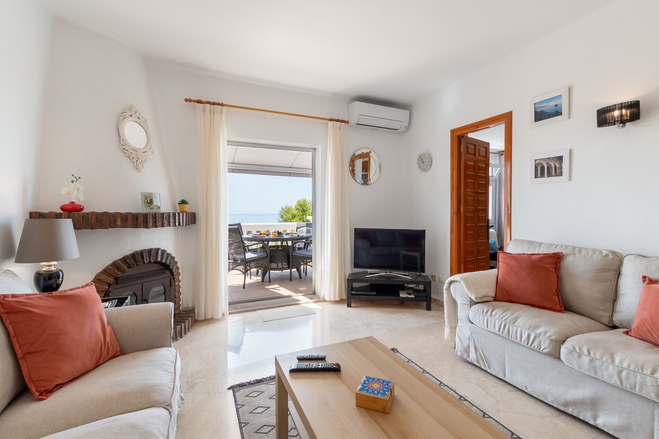 A living room with a sofa, a coffee table, a TV, and a fireplace. There is a door leading to an outdoor area with a table and chairs.