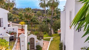 A white building with a balcony, surrounded by lush greenery and palm trees.