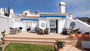 A white building with a blue awning, outdoor seating, and potted plants. - Tetuan 42 - El Oasis de Capistrano! (Nerja)