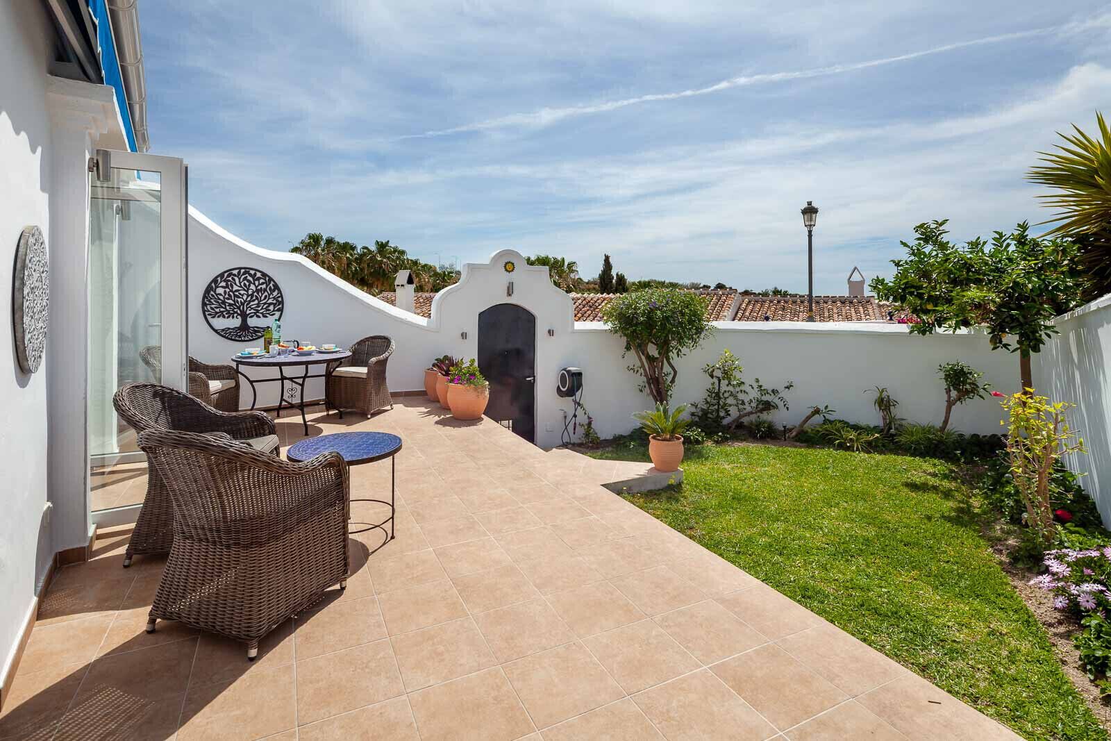 An outdoor patio with wicker furniture, a small table, and potted plants.