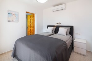 Un dormitorio con cama, mesitas de noche, un equipo de aire acondicionado y una puerta.