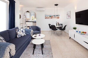 Una sala de estar moderna con sofá, mesa de centro, zona de comedor y cocina al fondo.