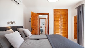 A bedroom with two beds, a wall-mounted air conditioner, and wooden doors. - Tetuan 42 - El Oasis de Capistrano! (Nerja)