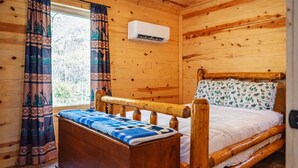 Une chambre dans une cabane en bois, avec un lit, des rideaux et un appareil de climatisation.