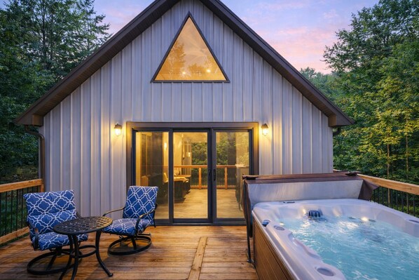 A modern cabin with a hot tub, wooden deck, and two rocking chairs.