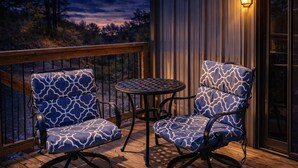 Une terrasse avec deux chaises et une table, entourée d’une rambarde en bois et offrant une vue sur les arbres.
