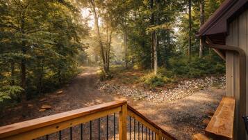 A forest path leading to a building with a wooden deck and railing.