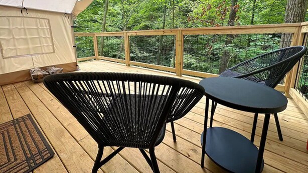 Un'area esterna coperta con un pavimento in legno, due poltrone in vimini nero e un tavolino.