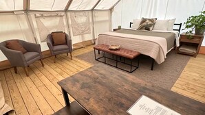 Una stanza con tende, un letto, due poltrone, un tavolo in legno e una panca.