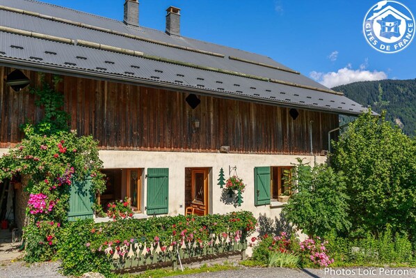 Traditional chalet with a rustic facade, surrounded by a well-maintained garden and a mountain view.