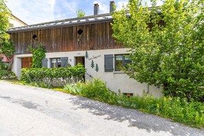 Un edificio rústico con fachada de madera, un letrero que dice 'Les Sapins', y un jardín con diversas plantas y una valla.