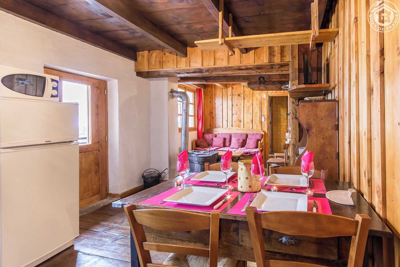 Un coin repas en bois avec une table dressée pour quatre personnes, un réfrigérateur et un espace salon confortable avec un canapé et des coussins.