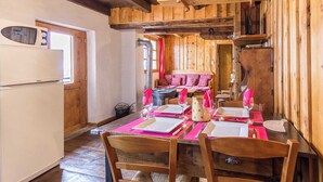 Un coin repas en bois avec une table dressée pour quatre personnes, un réfrigérateur et un espace salon confortable avec un canapé et des coussins.