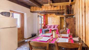 Un coin repas en bois avec une table dressée pour quatre personnes, un réfrigérateur et un espace salon confortable avec un canapé et des coussins.