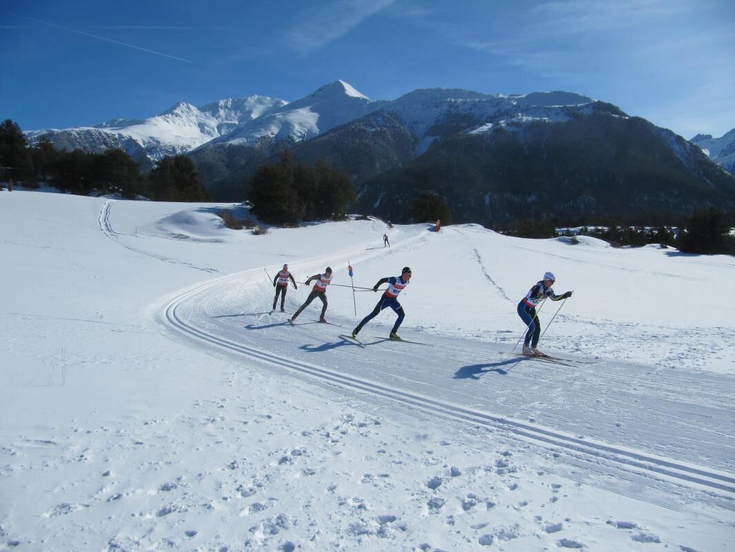 A group of cross-country skiers on a snowy trail with mountains in the background.