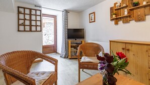 Ein Zimmer mit Korbstühlen, einem Holztisch mit Blumenvase, einem Fernseher und einem Holzregal mit Dekoration.