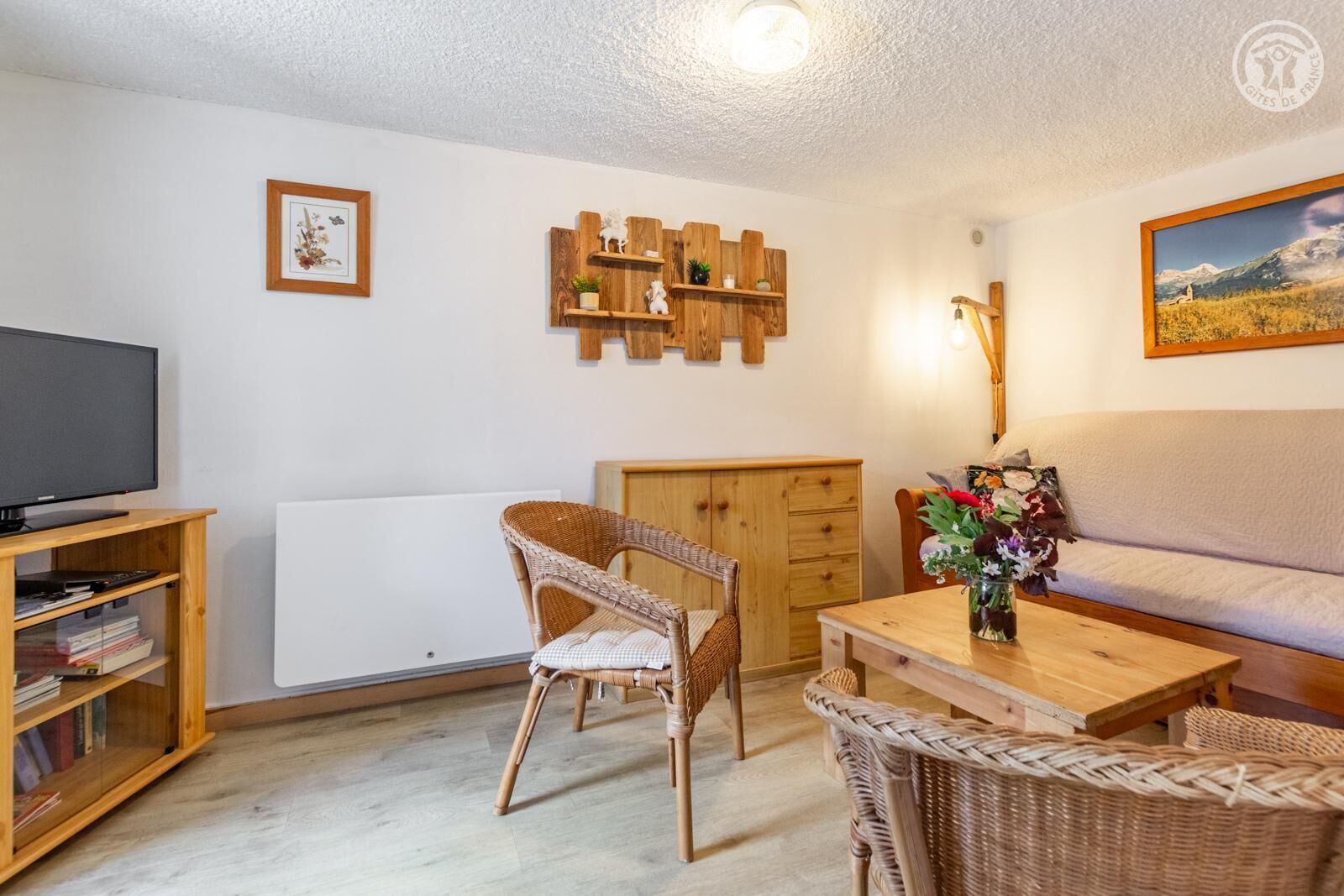 Un salon avec un téléviseur, des meubles en osier, une étagère en bois et un tableau accroché au mur.