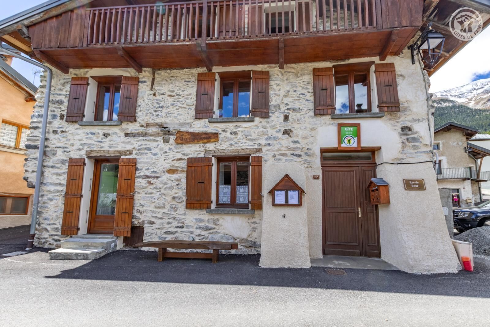 A stone building with wooden shutters, a sign indicating it's a Gîte, and a plaque reading 'Rac du Four.'