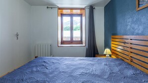 Ein Schlafzimmer mit Bett, Fenster mit Vorhängen, Heizkörper und einem Holzkopfteil.