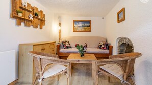 Ein gemütlicher Raum mit einer Couch, zwei Korbstühlen, einem Holztisch, einem Kamin und einem an der Wand befestigten Regal mit Dekoration.