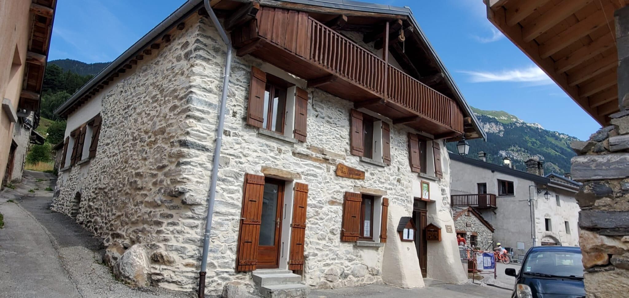 Un edificio de piedra con contraventanas de madera y un balcón, situado en una zona montañosa.