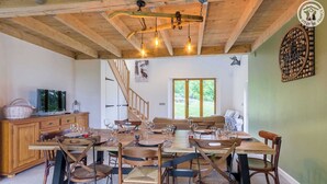 A dining area with a wooden table set for six, surrounded by wicker chairs. A staircase leads to an upper level. - LA BERGERIE DE CLAUDE (LE BOURGET DU LAC)