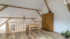A loft bedroom with exposed wooden beams, a wooden table, a bench, a wardrobe, and a hanging light fixture. - LA BERGERIE DE CLAUDE (LE BOURGET DU LAC)