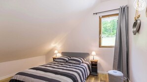 A bedroom with a bed, two bedside tables with lamps, a window with curtains, and a small ottoman. - LA BERGERIE DE CLAUDE (LE BOURGET DU LAC)