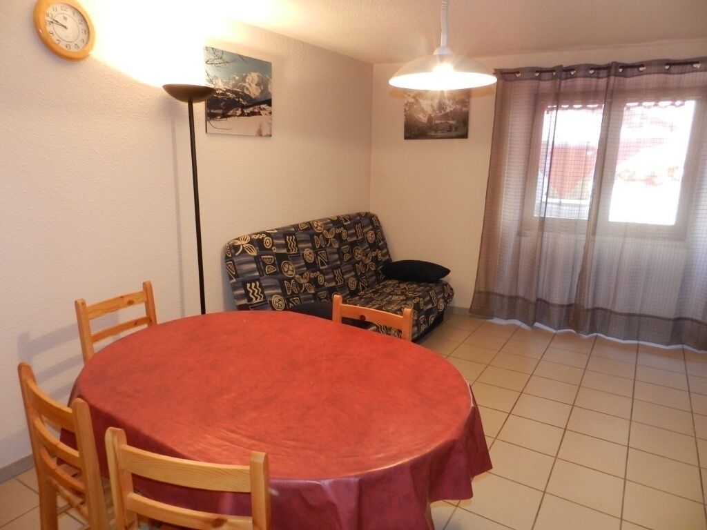 A dining area with a round table and chairs, a sofa, a clock, and two paintings on the wall.