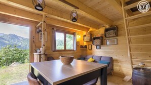 L’intérieur d’un chalet chaleureux, avec une table en bois, des chaises, un canapé et une bibliothèque.