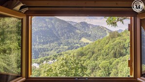 Une fenêtre à cadre en bois donnant sur un paysage montagneux.