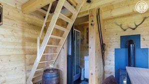 L’intérieur d’un chalet en bois, avec un escalier en bois, un tonneau, une porte bleue et une cheminée.