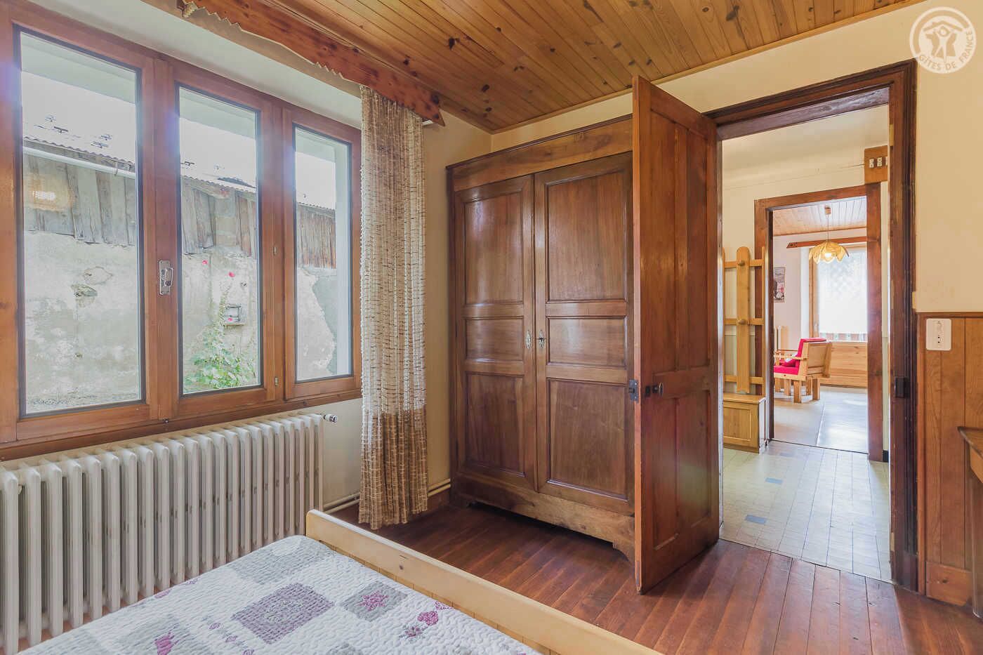 A room with a wooden floor, a large wardrobe, a radiator, and a window with curtains.
