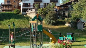 A playground with climbing structures and a slide, surrounded by houses and greenery. - LES GENTIANES - REGUET (NOTRE DAME DE BELLECOMBE)