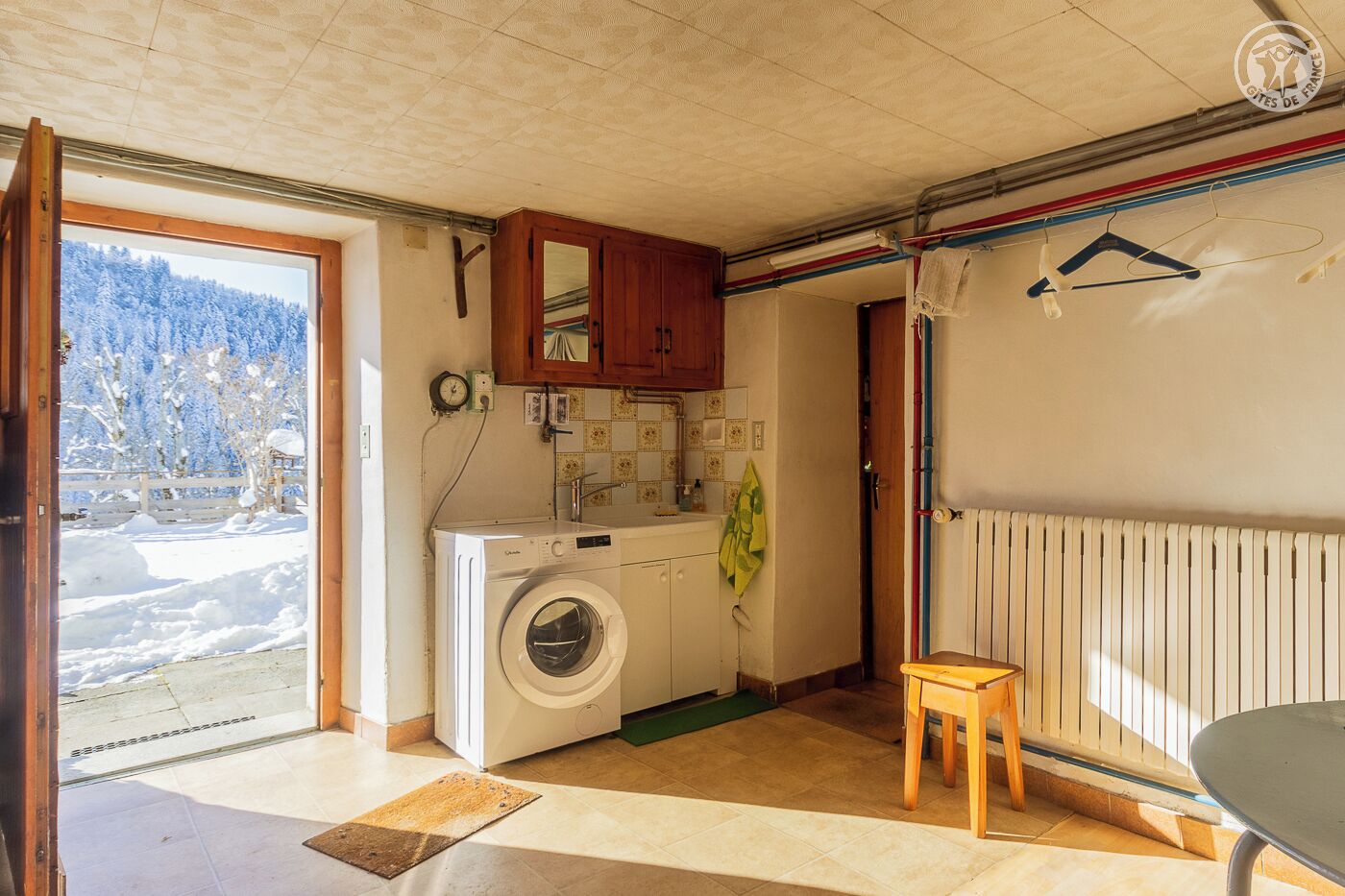 Eine kompakte Küche mit Waschmaschine, einem kleinen Tisch und Blick auf eine verschneite Landschaft durch eine offene Tür.