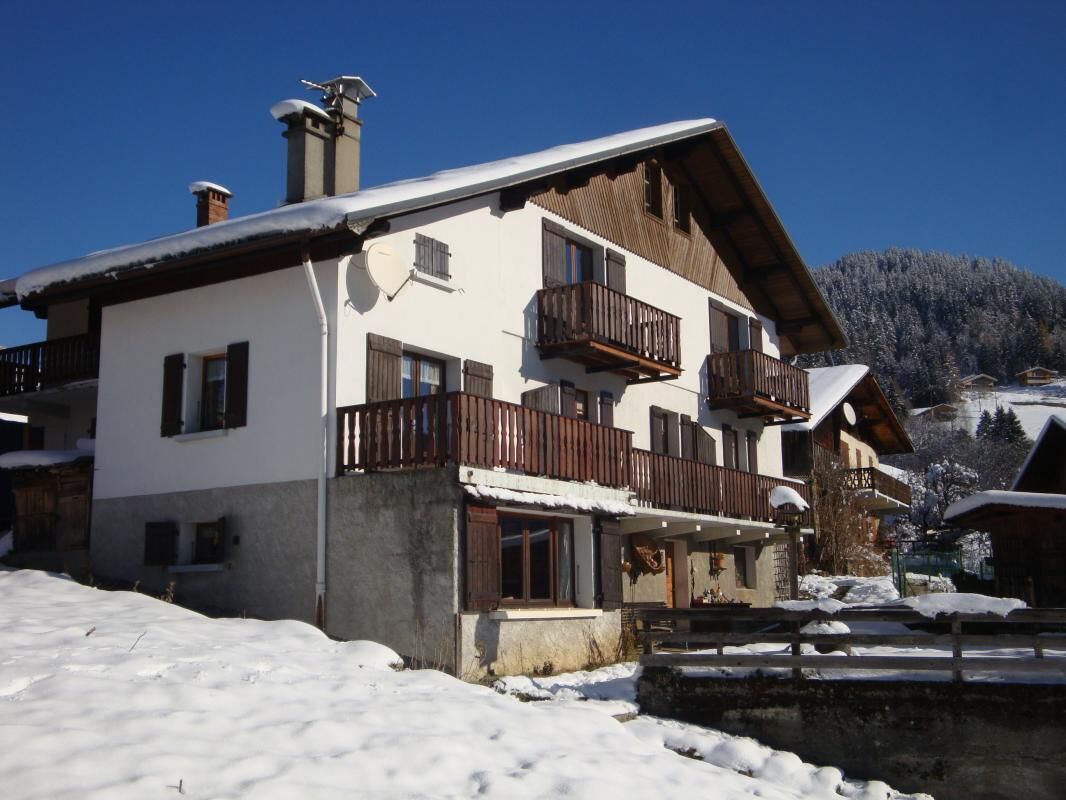 Een chalet met twee verdiepingen, houten balkonnes, een stenen fundering en een met sneeuw bedekte dak.