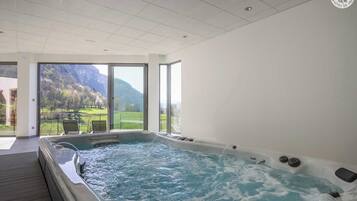 A modern indoor hot tub with a view of a mountainous landscape through large windows.