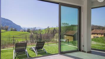 A modern room with large glass windows offering a view of a green landscape and mountains.