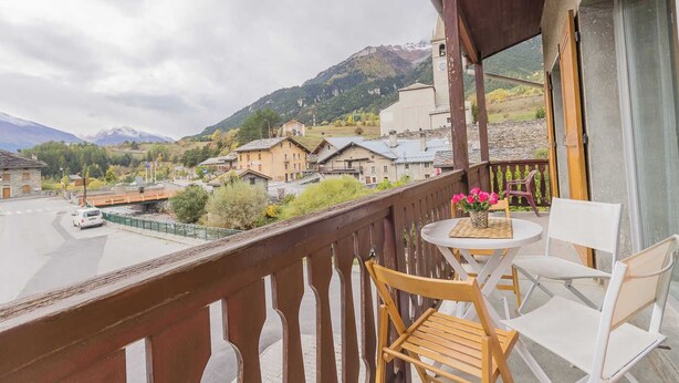 Un balcon donnant sur un village, une table avec des chaises et une rambarde en bois.