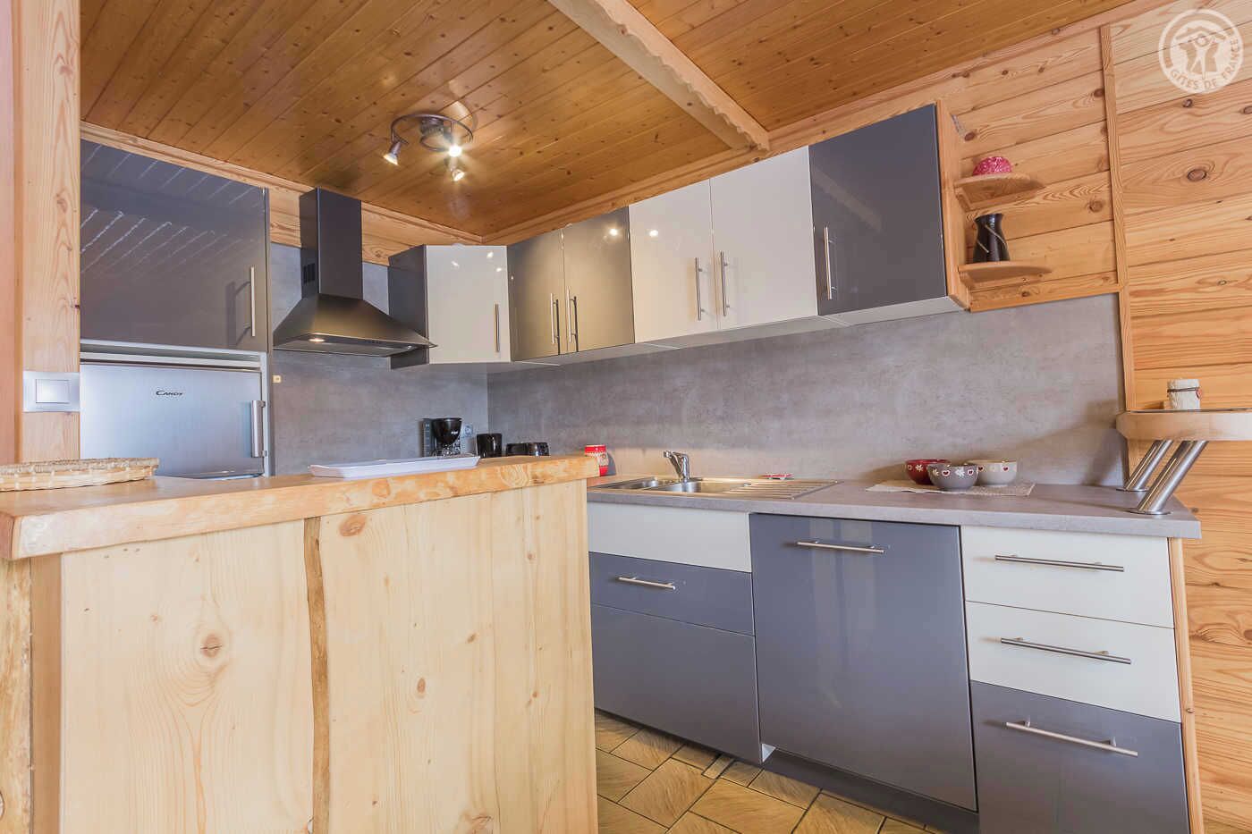Une cuisine moderne avec des meubles en bois, un réfrigérateur en acier inoxydable et un plan de travail gris.