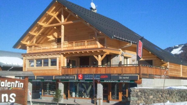 A wooden lodge with a balcony, ski rental sign, and a sign for 'Valentin'.