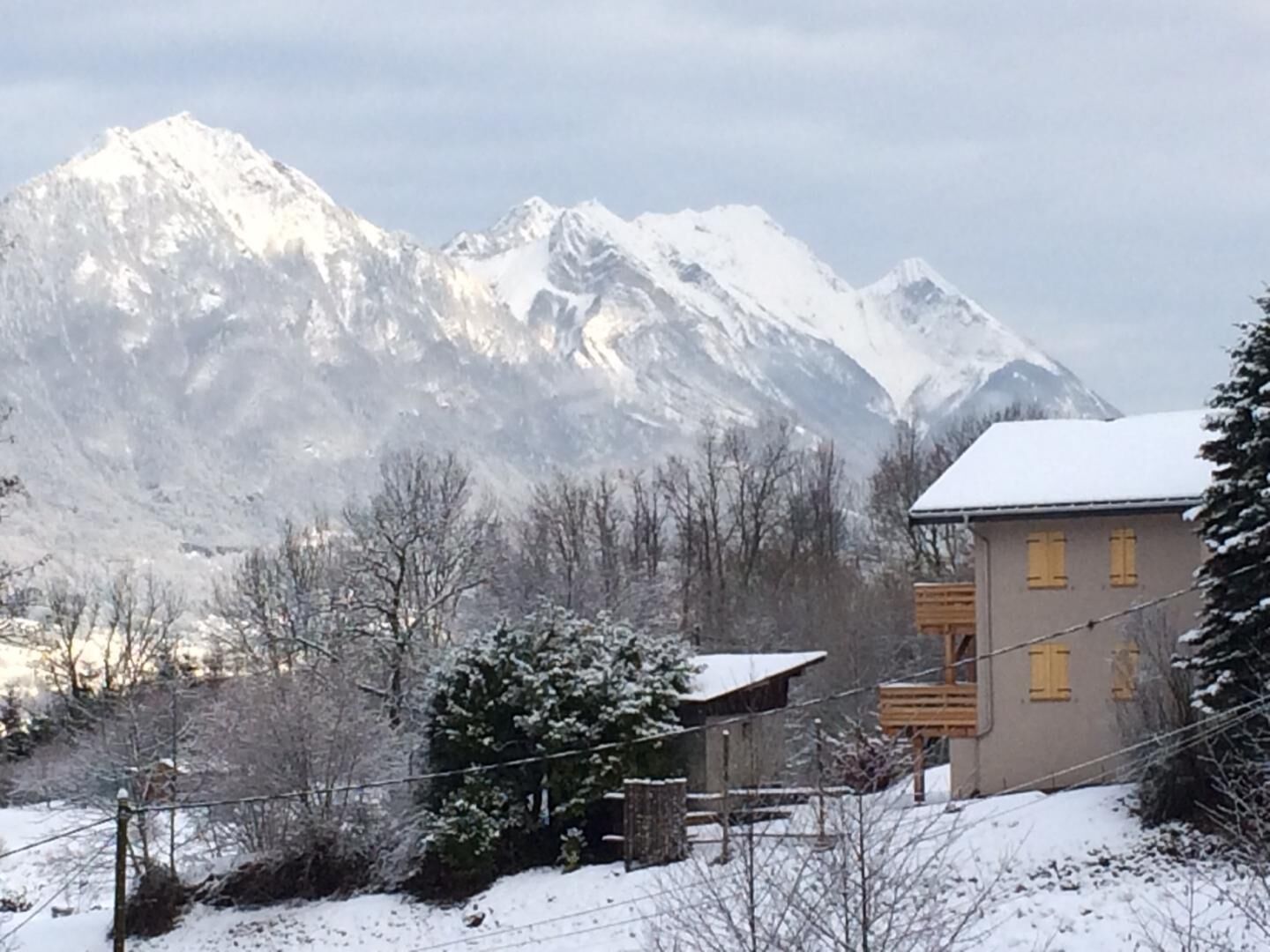 A mountain cabin with a wooden balcony, surrounded by snow-covered trees and mountains in the background.
