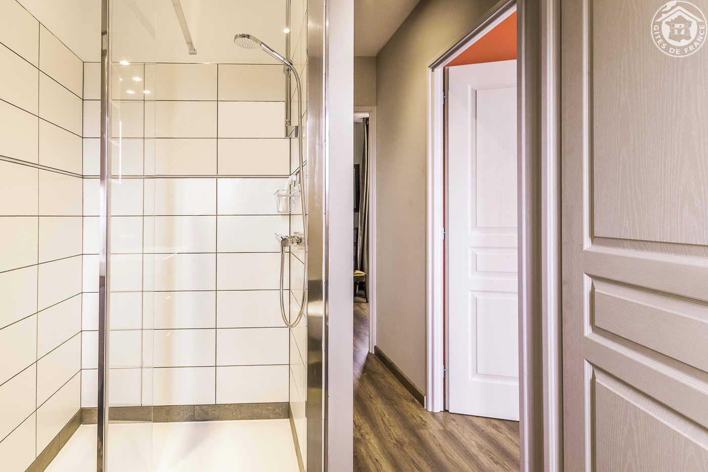 A modern bathroom with a glass shower enclosure, tiled walls, and a wooden floor.