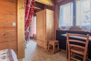 A wooden cabin interior with a dining area, a small stool, and a cabinet.