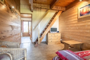 A wooden interior with a staircase, a TV on a dresser, wicker furniture, and a framed picture on the wall.
