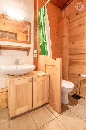 Baño de cabaña de madera con lavamanos, inodoro y cortina de ducha.