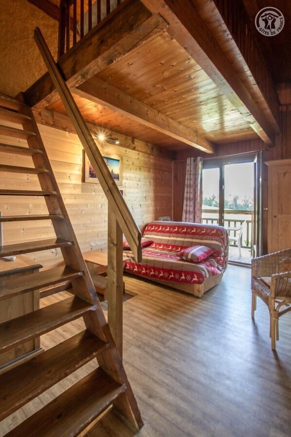 Una escalera de madera que lleva a un balcón con una cama y muebles de mimbre.