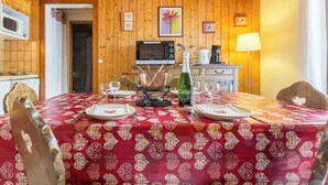 Un comedor con paredes de madera, una mesa dispuesta con platos, vasos y una botella de vino. Hay un microondas y una cafetera en la encimera.