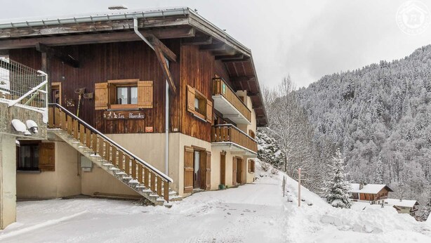 Una cabaña de madera con una escalera de madera que lleva a un balcón, rodeada de árboles cubiertos de nieve.