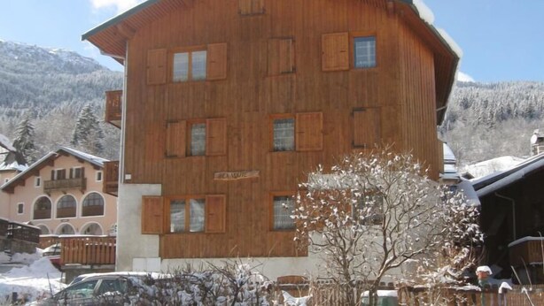 Een meerlaags houten gebouw met een schuin dak, waarschijnlijk een hotel of lodge, omgeven door met sneeuw bedekte bomen en bergen op de achtergrond.